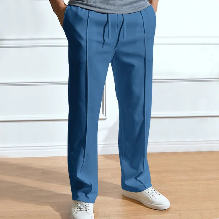 Pantalon bleu denim à taille élastique et plis marqués, porté avec un t-shirt gris et des baskets blanches. 5