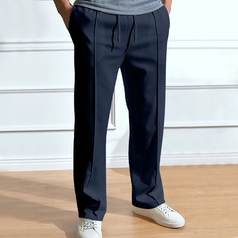 Pantalon bleu marine à cordon et pinces marquées, porté avec un t-shirt gris et des baskets blanches. 1