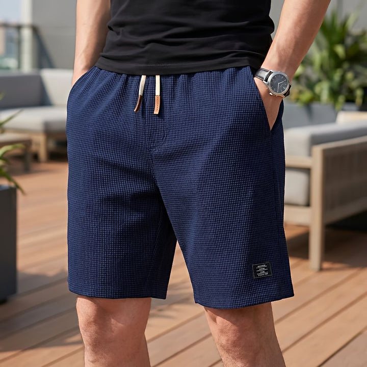 Short bleu marine en tissu gaufré à cordon clair, porté avec un tee-shirt noir, une main dans la poche, sur une terrasse. 7