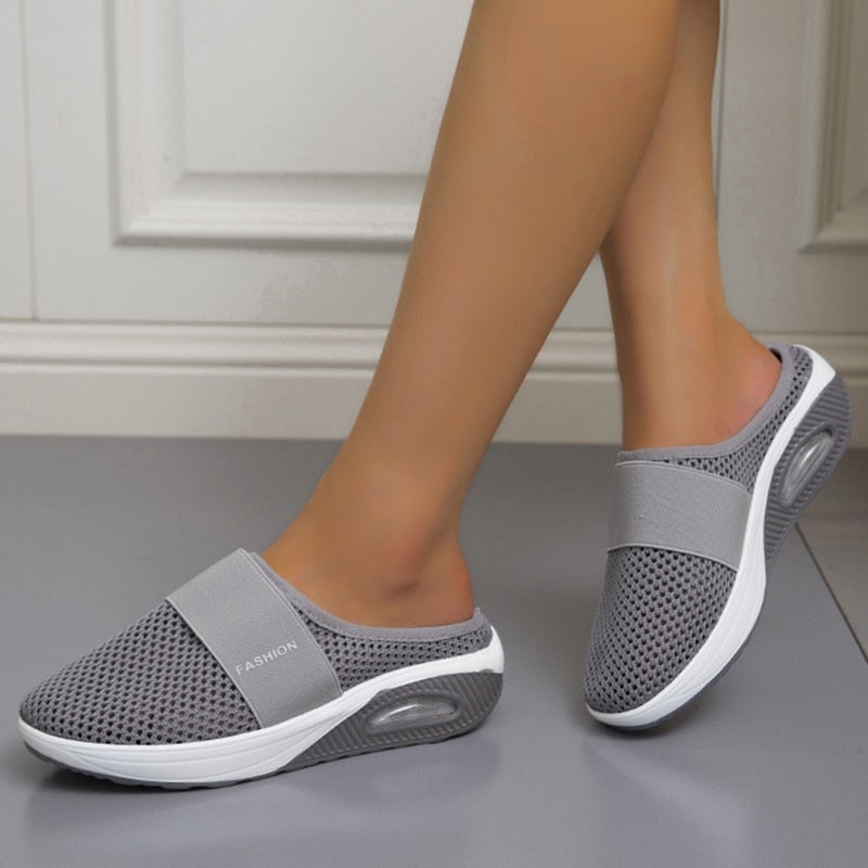 Paire de mules grises en maille portées par une femme, vue de profil sur un sol gris 2