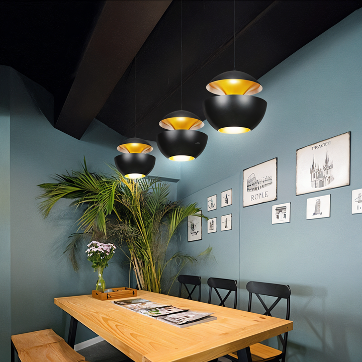 Trois suspensions noires Г  l'intГ©rieur dorГ© au-dessus d'une table en bois, dans une salle Г  manger aux murs bleu-gris. 2