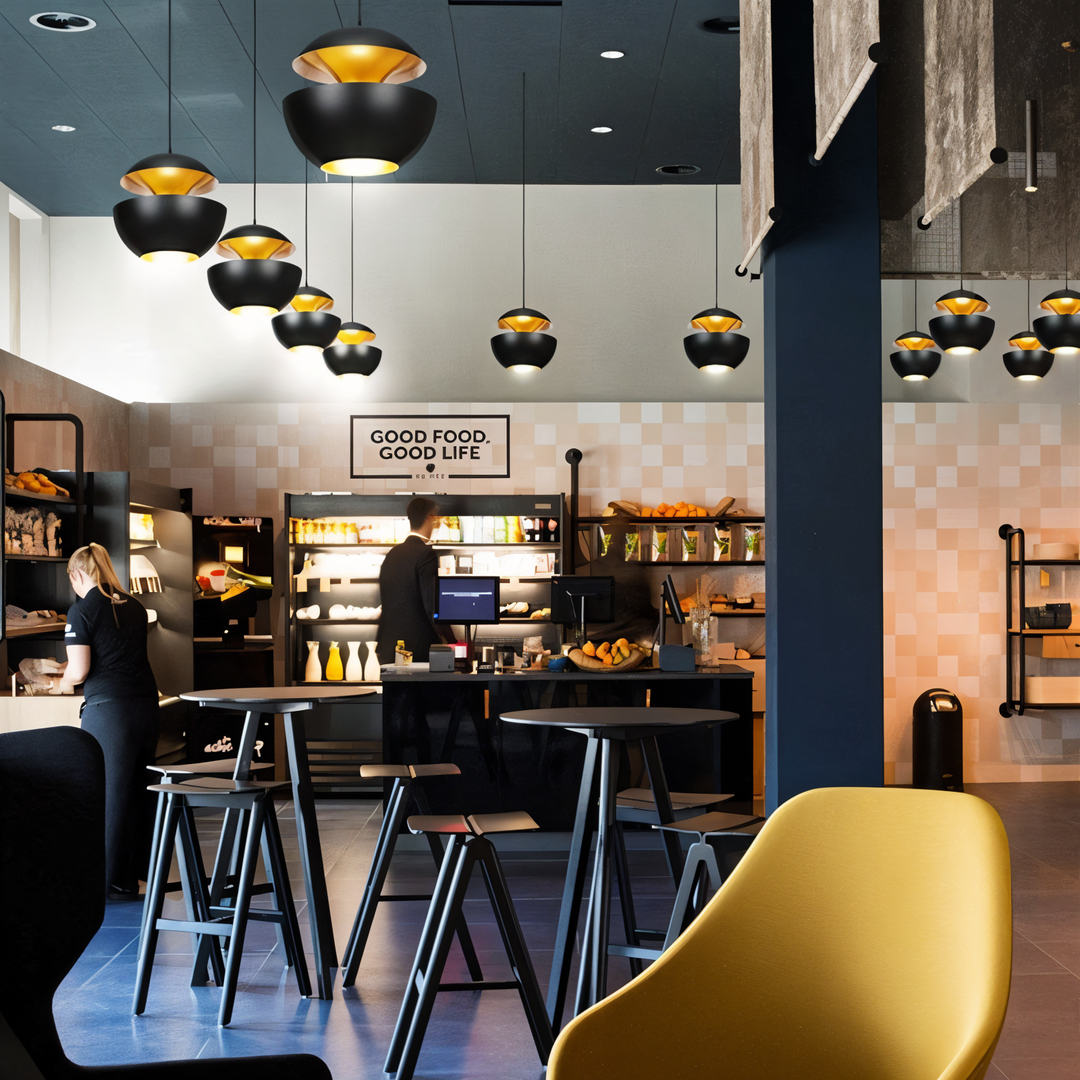 Nombreuses suspensions noires et dorГ©es de tailles variГ©es dans un cafГ©-boutique moderne avec tables hautes et fauteuil jaune. 4