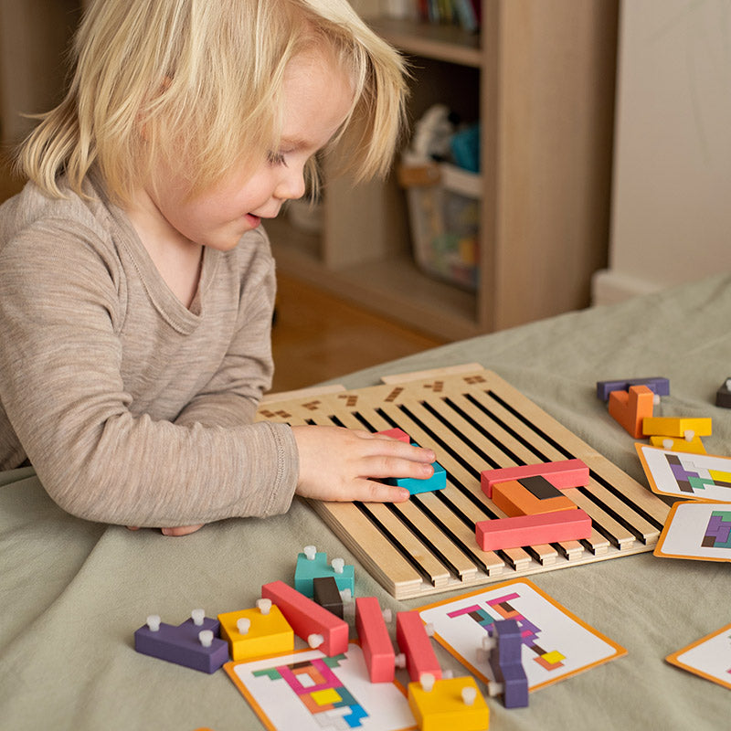Petit garçon blond souriant qui assemble les pièces sur le plateau en bois, entouré de cartes modèles et de pièces à picots. 4