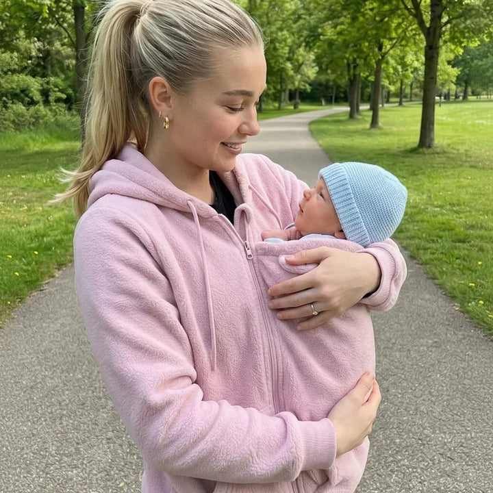 Femme en sweat rose polaire dans un parc, regardant son bébé en bonnet bleu porté contre elle. 4