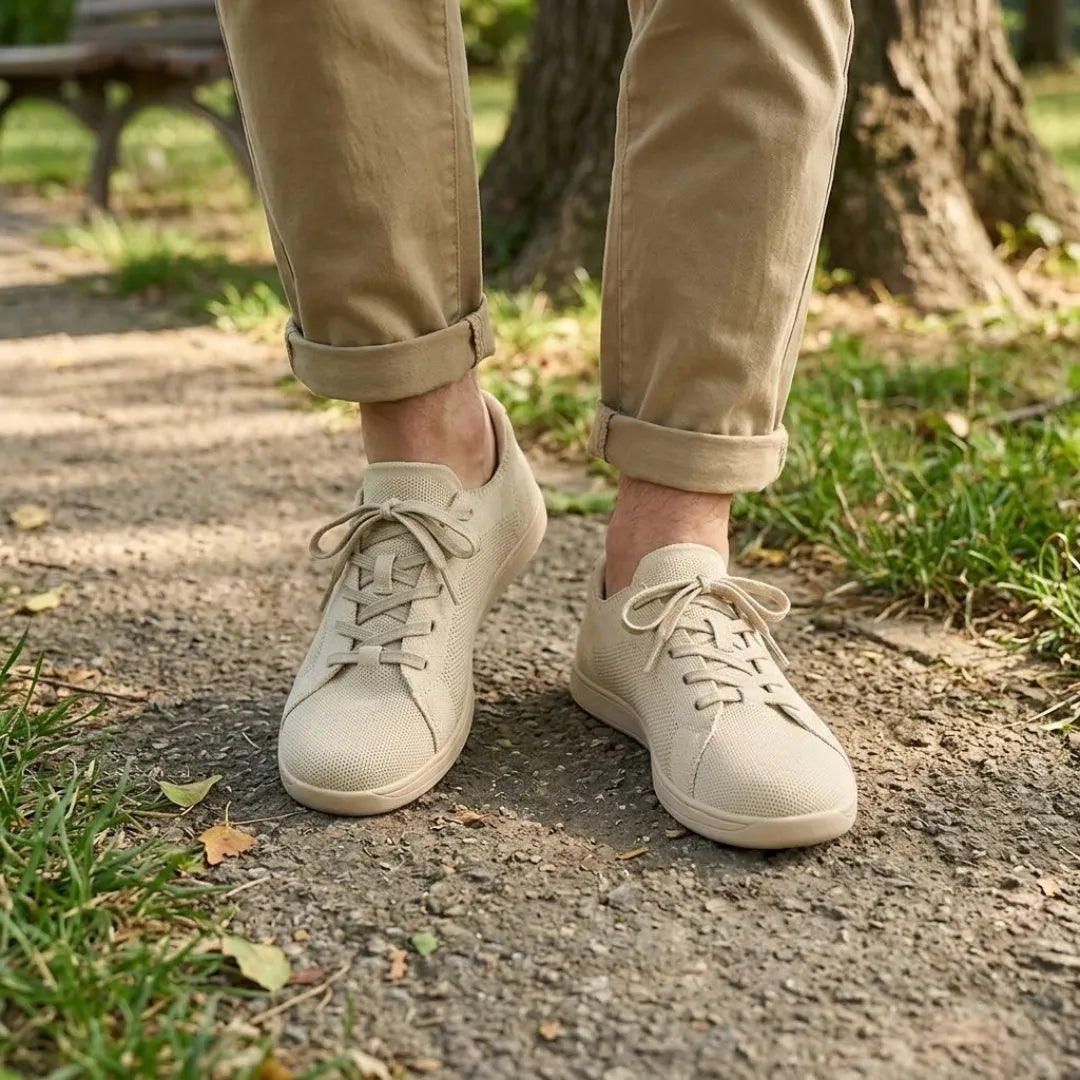 Pieds portant les baskets beiges sur un chemin de parc, avec un pantalon chino beige retroussé et de l'herbe autour. 2