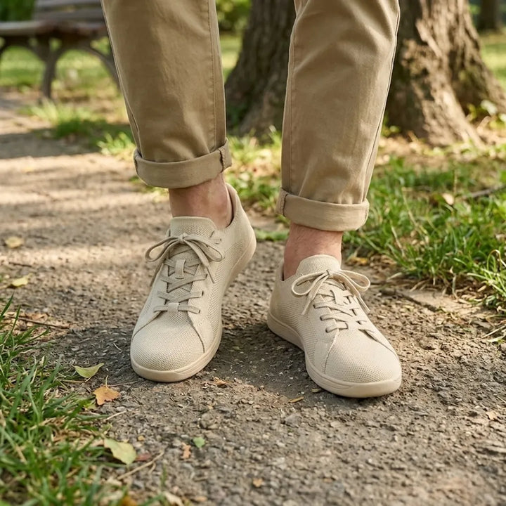Pieds portant les baskets beiges sur un chemin de parc, avec un pantalon chino beige retroussé et de l'herbe autour. 2