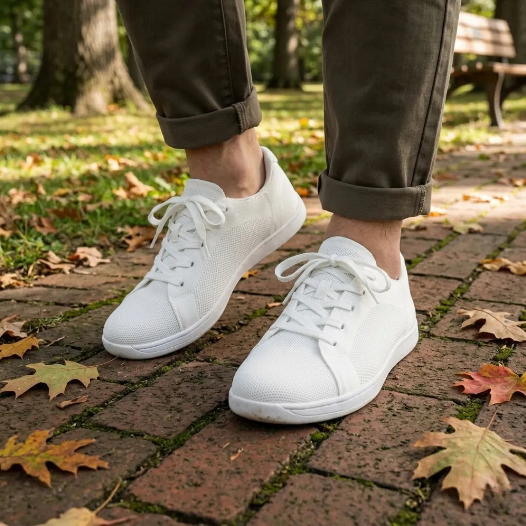 Pieds d'une personne en pantalon kaki retroussé portant les baskets blanches, sur un chemin pavé parsemé de feuilles d'automne. 38