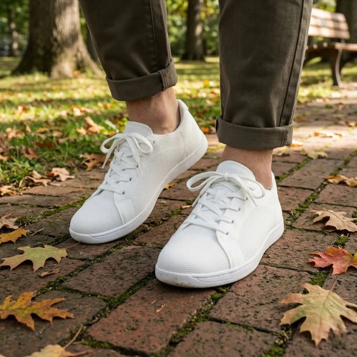Pieds d'une personne en pantalon kaki retroussé portant les baskets blanches, sur un chemin pavé parsemé de feuilles d'automne. 38
