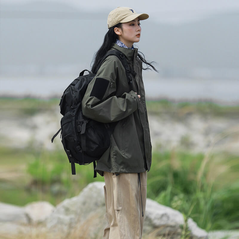 Femme de profil en veste vert kaki, pantalon beige et sac à dos noir, debout parmi les rochers. 4