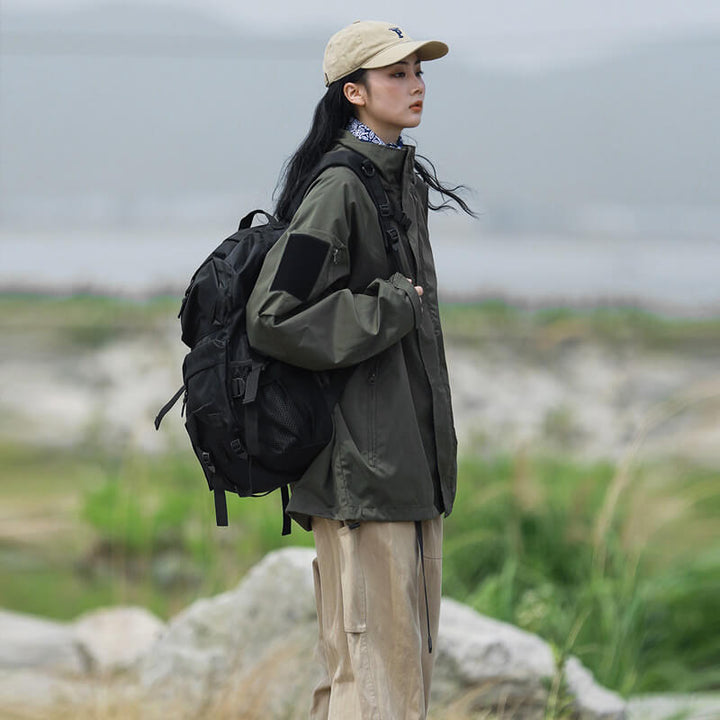 Femme de profil en veste vert kaki, pantalon beige et sac à dos noir, debout parmi les rochers. 4