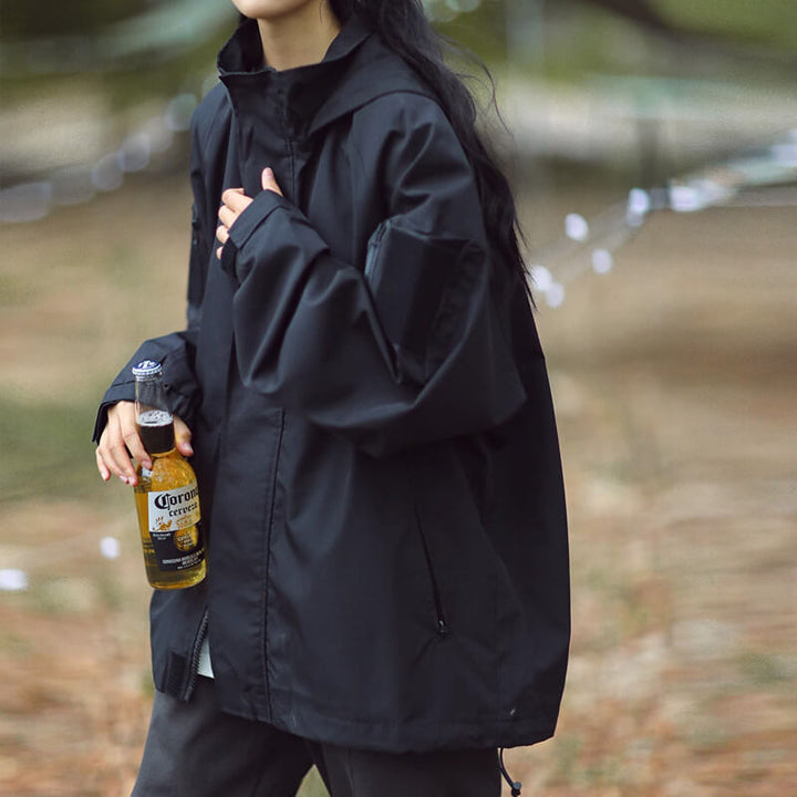Femme en veste noire à capuche vue de côté, poche zippée sur le devant, tenant une bouteille de bière. 7