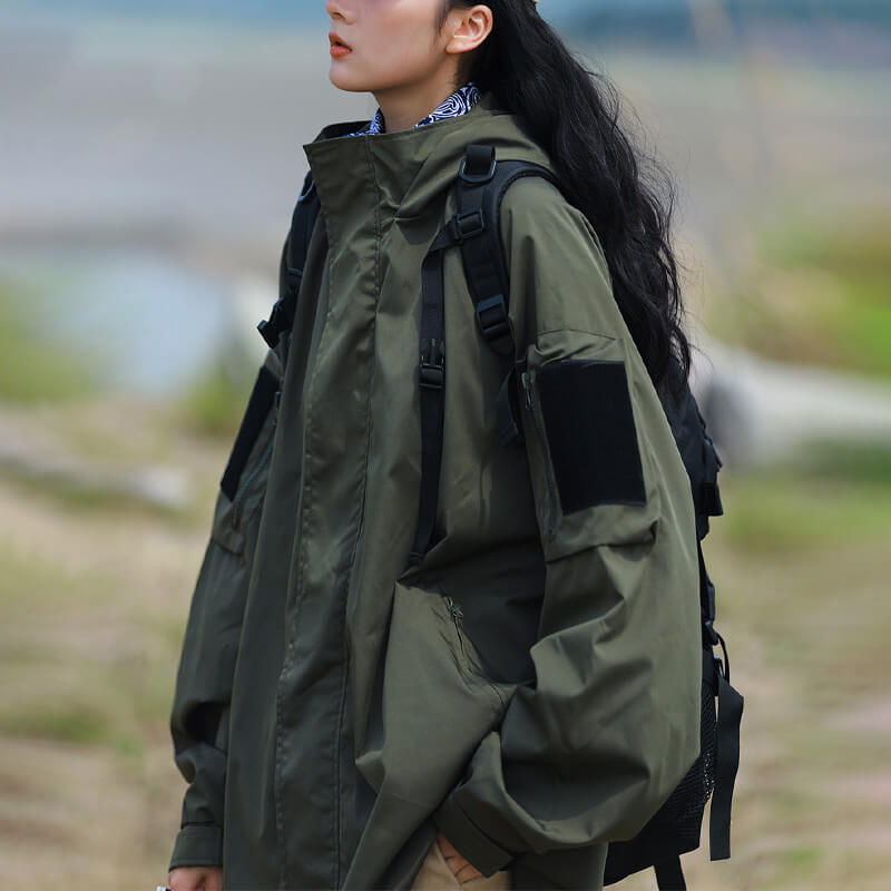 Femme en veste vert kaki à col montant, poche de manche à scratch et poche zippée, sac à dos sur les épaules. 8