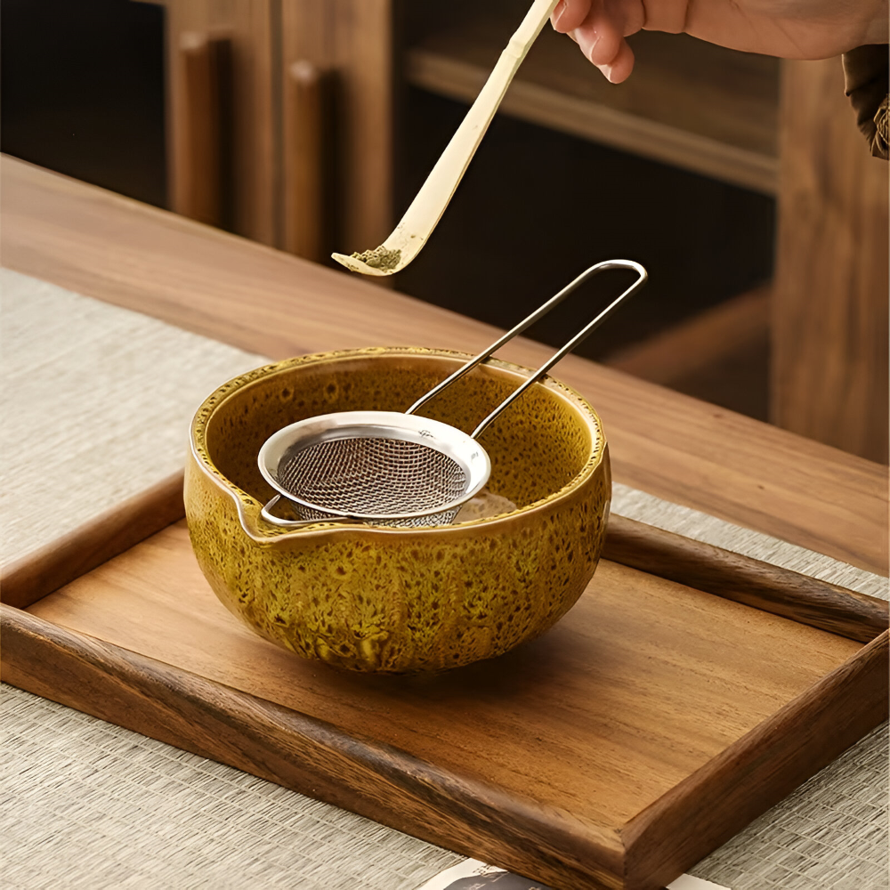 Cuillère en bambou chargée de poudre de matcha au-dessus de la passoire inox posée sur le bol jaune moucheté. 8