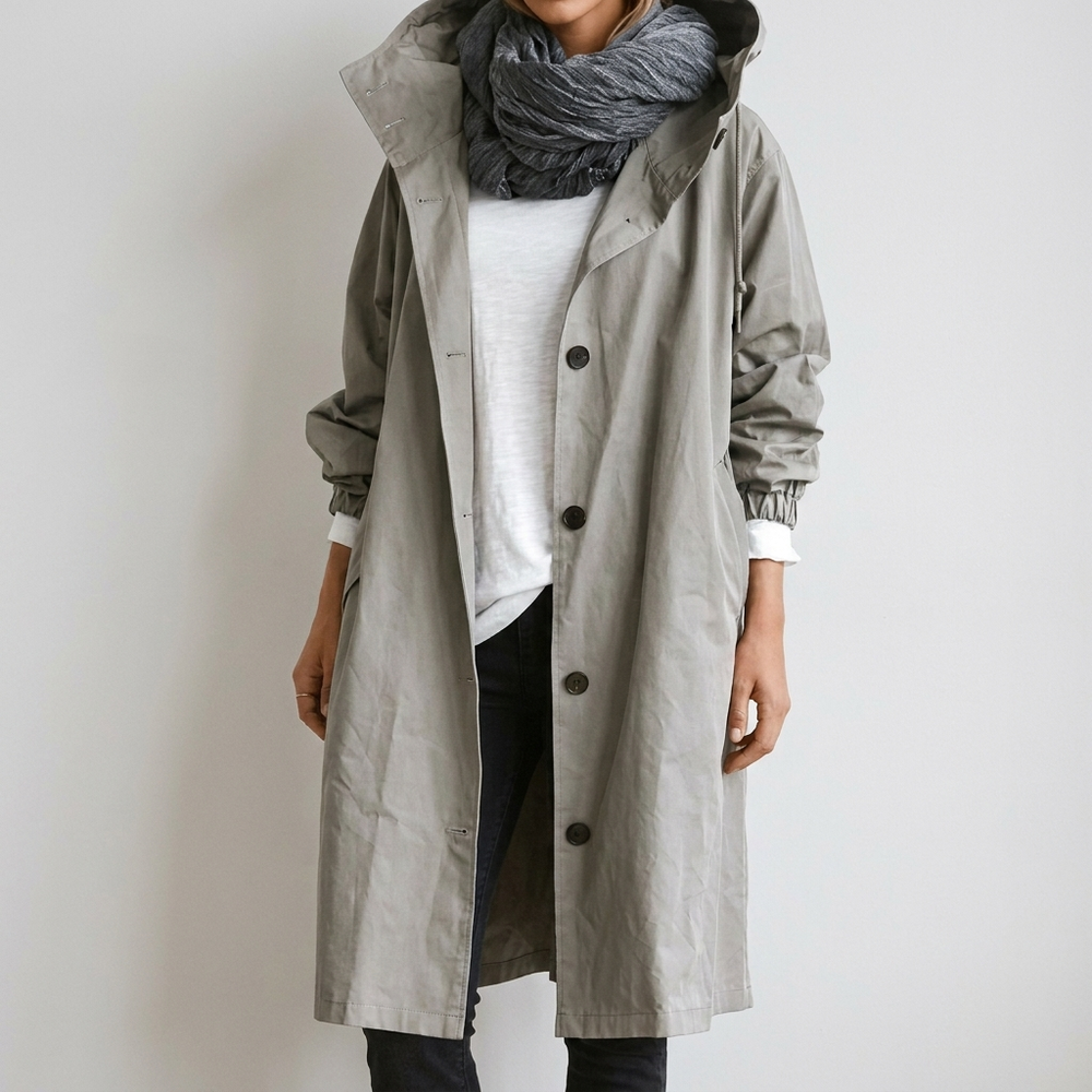 Imperméable long gris clair à capuche, boutonné devant, porté ouvert sur un t-shirt blanc et une écharpe grise. 2
