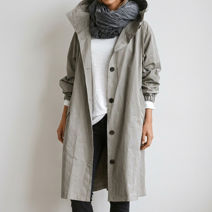 Imperméable long gris clair à capuche, boutonné devant, porté ouvert sur un t-shirt blanc et une écharpe grise. 2