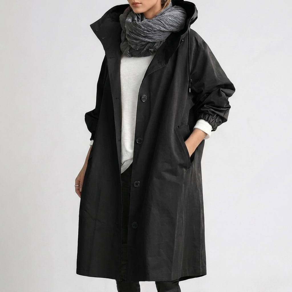 Imperméable long noir à capuche, porté avec une écharpe grise, une main dans la poche, sur fond clair. 3