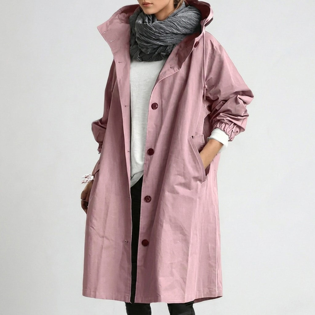 Imperméable long rose à capuche et boutons, porté avec écharpe grise, main dans la poche, sur fond clair. 1