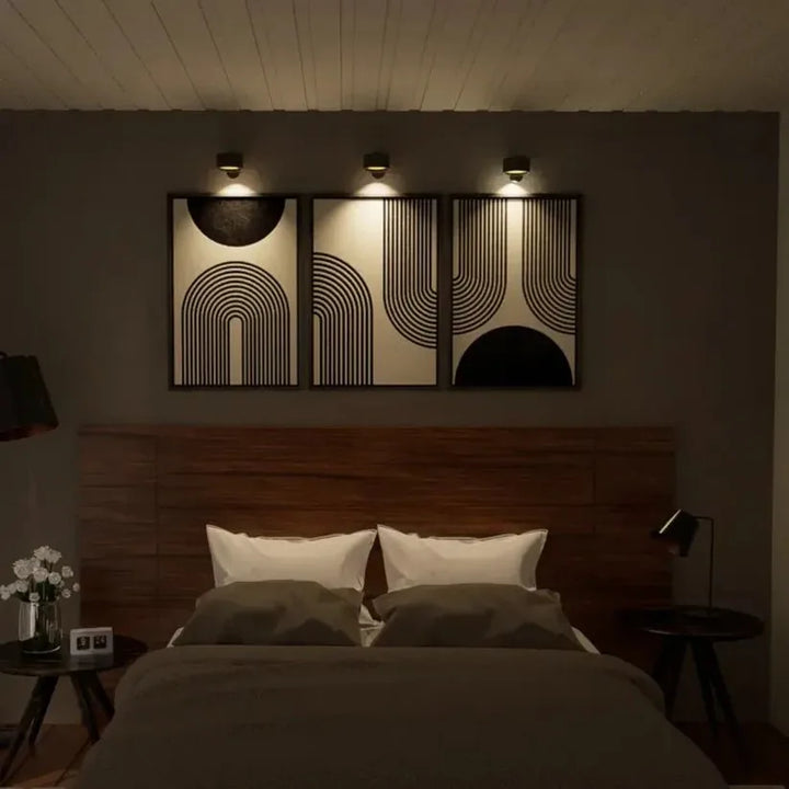 Trois lampes murales noires allumées éclairant trois tableaux graphiques au-dessus d'un lit dans une chambre sombre 10