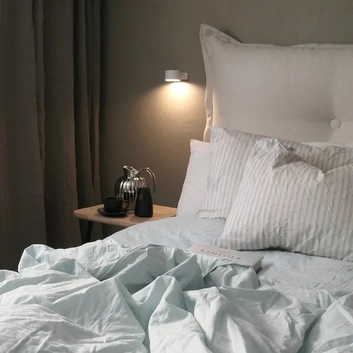 Lampe murale blanche allumée au-dessus d'un lit au linge clair, avec plateau de boissons sur la table de chevet 12