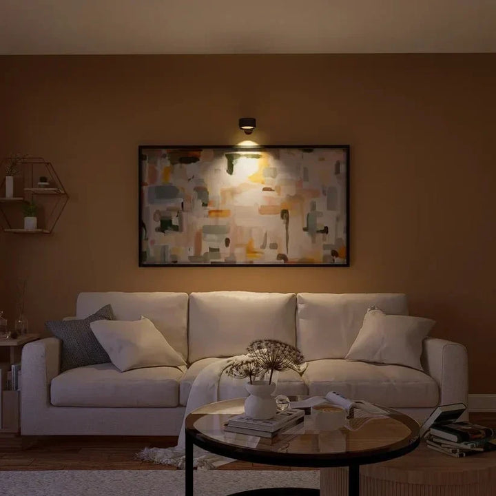 Lampe murale noire allumée au-dessus d'un tableau coloré et d'un canapé clair dans un salon feutré 15
