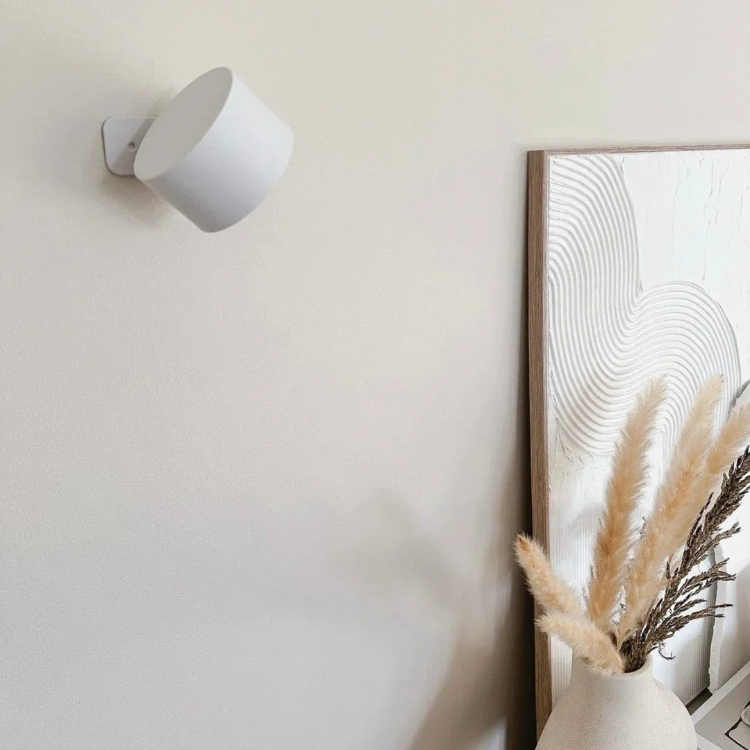 Lampe murale blanche éteinte, tête inclinée, fixée au mur près d'un tableau texturé et d'un vase de pampa 16