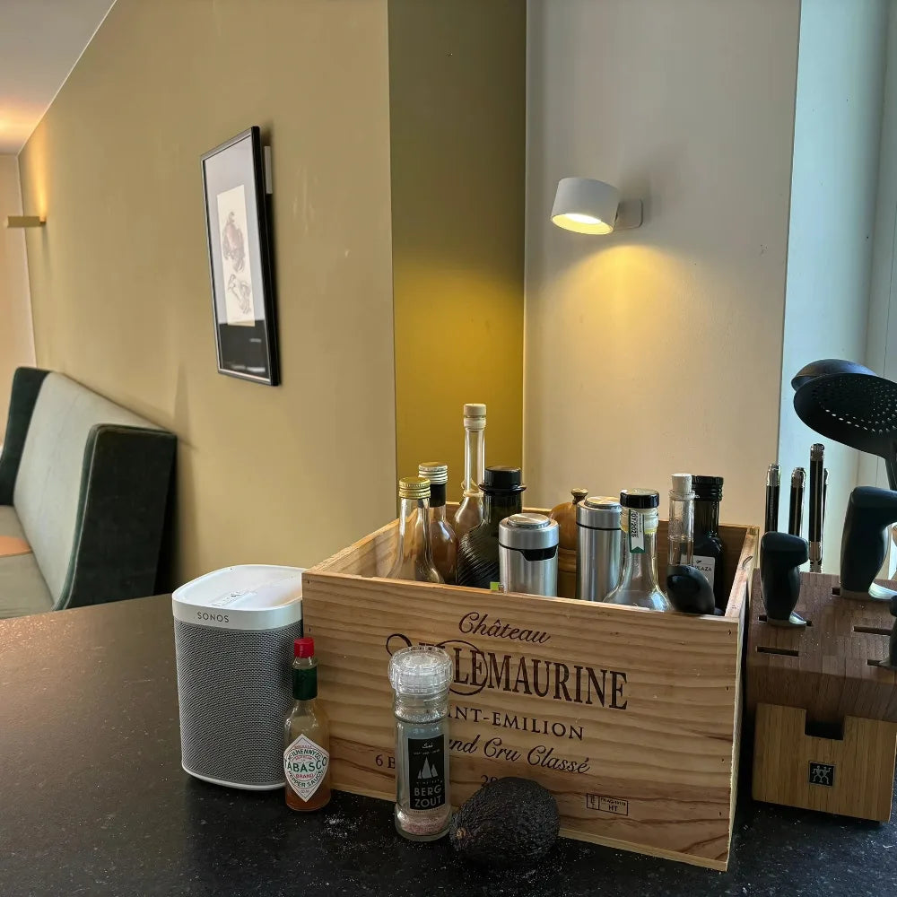 Lampe murale blanche allumée au-dessus d'un plan de travail de cuisine avec caisse en bois et bouteilles 2