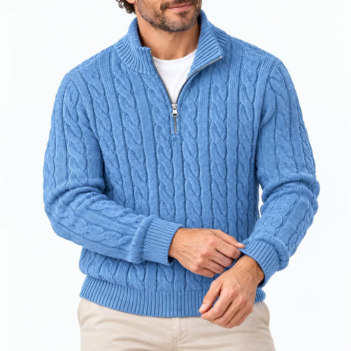 Homme portant le pull bleu à torsades et demi-zip, mains croisées devant lui, sur fond blanc, gros plan buste. 1