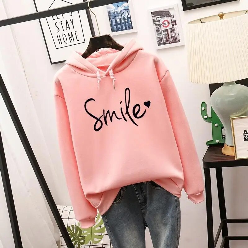 Sweat à capuche rose clair suspendu, cordons à la capuche, motif noir manuscrit avec cœur sur la poitrine, porté avec un jean. 2