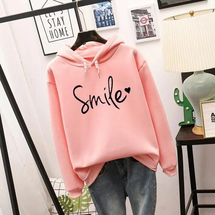 Sweat à capuche rose clair suspendu, cordons à la capuche, motif noir manuscrit avec cœur sur la poitrine, porté avec un jean. 2