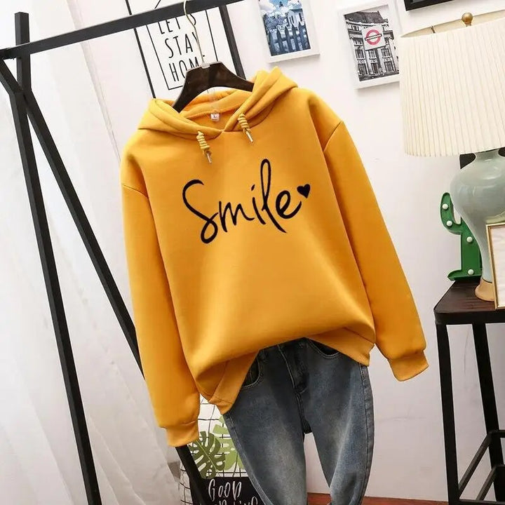Sweat à capuche jaune moutarde suspendu sur cintre, manches longues à poignets côtelés, motif noir avec cœur, jean en dessous. 4