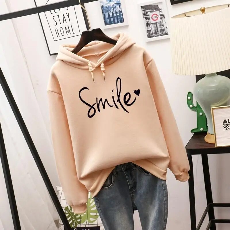Sweat à capuche beige sur cintre, avec cordons de serrage et motif noir en lettres cursives et petit cœur, devant un jean. 1