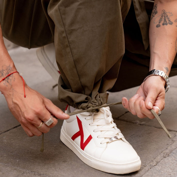 Détail de la cheville du pantalon kaki que l'on resserre en tirant le cordon de serrage, au-dessus d'une basket blanche. 5
