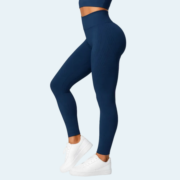 Femme de profil en leggings bleu marine taille haute lisses, jambe pliée, avec baskets blanches sur fond bleu clair. 4