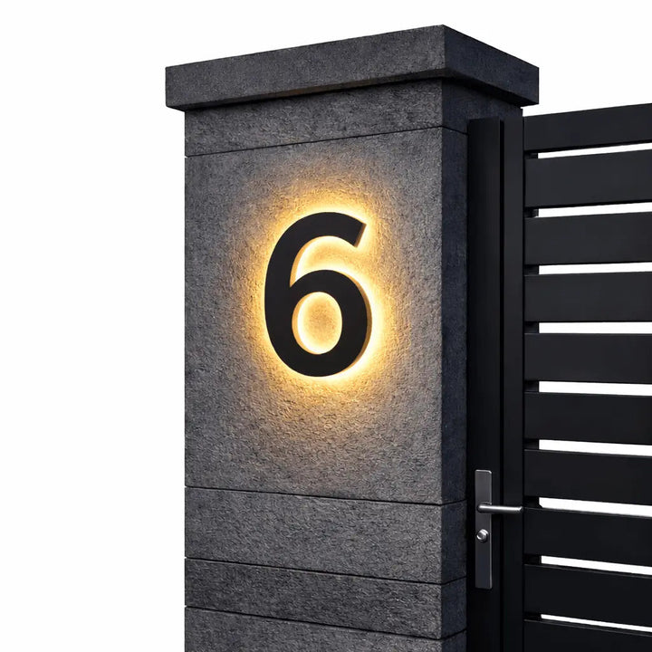 Chiffre 6 noir rétroéclairé d'une lueur chaude, fixé sur un pilier en pierre sombre à côté d'un portail, fond blanc. 6
