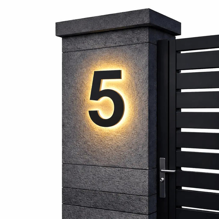 Chiffre 5 noir rétroéclairé d'une lumière chaude sur un pilier en pierre grise, portail noir à lames à droite, fond blanc. 7