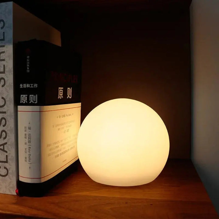 Orbe allumé en lumière chaude sur une étagère en bois, calé contre un livre en guise de veilleuse. 4