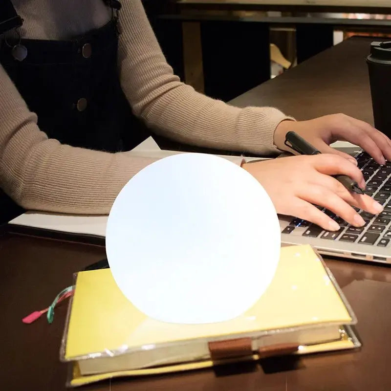 Orbe allumé en lumière blanche posé sur un carnet jaune, devant une personne qui tape sur un ordinateur portable. 7