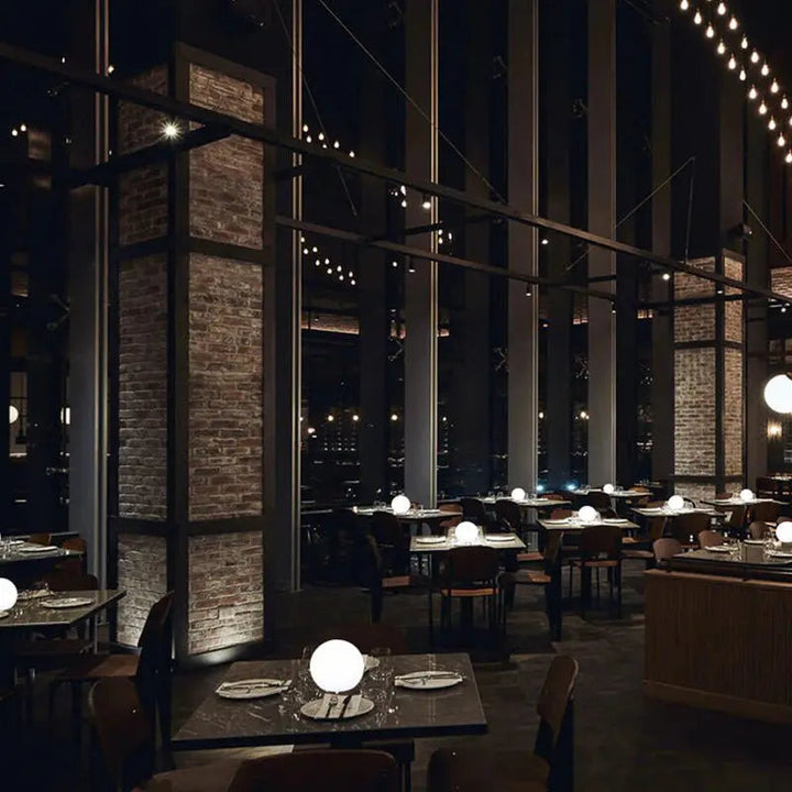Plusieurs orbes lumineux posés sur les tables d'une grande salle de restaurant sombre aux murs de briques. 8