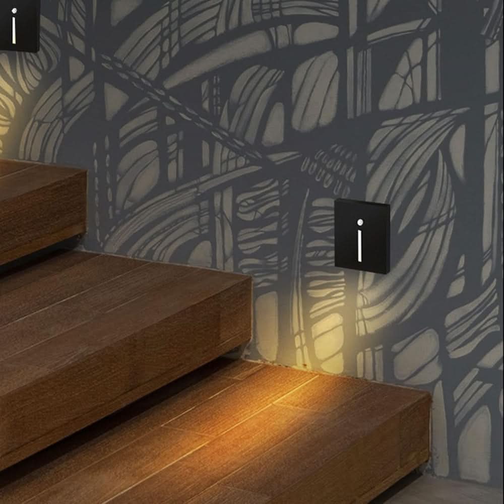 Deux appliques noires à fente lumineuse sur un mur à motifs, éclairant des marches en bois 2