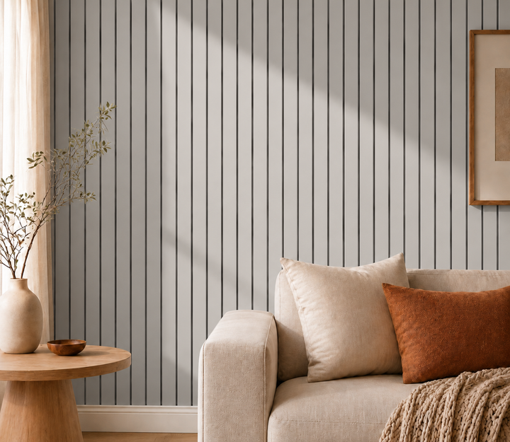 Gros plan sur un mur de lattes grises et rainures sombres, avec canapé beige et coussin rouille 16