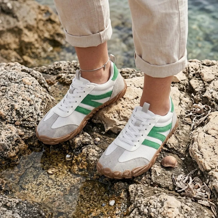 Pieds d'une femme portant les baskets blanches à bandes vertes sur des rochers au bord de l'eau, pantalon de lin retroussé. 29