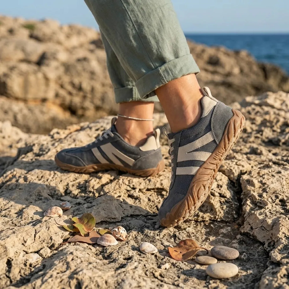 Pieds portant les chaussures grises, pantalon vert retroussé, posés sur des rochers au bord de la mer avec coquillages. 2