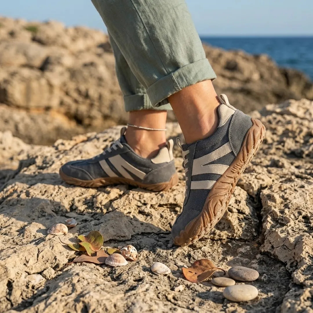 Pieds portant les chaussures grises, pantalon vert retroussé, posés sur des rochers au bord de la mer avec coquillages. 2