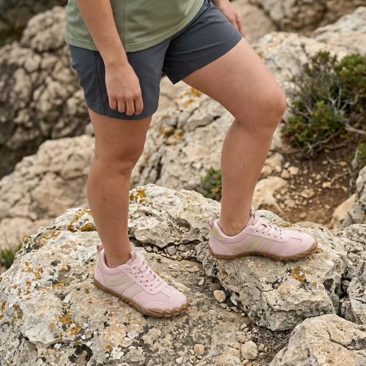 Femme en short gris et haut vert portant les chaussures roses, un pied posé sur un rocher couvert de lichens. 11