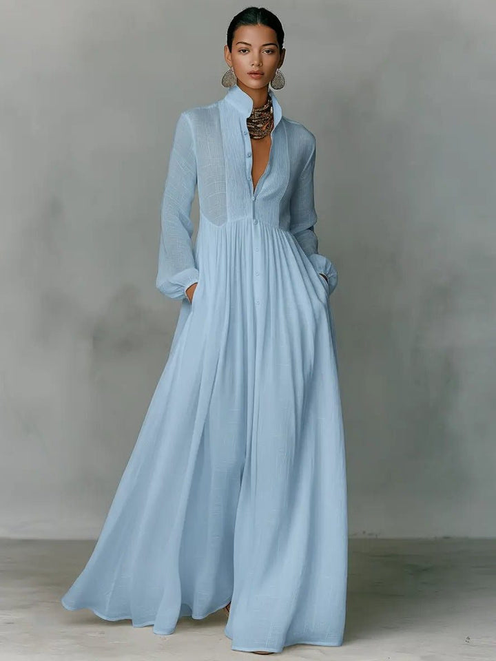 Robe maxi bleu ciel portée de face avec collier et boucles d'oreilles, mains dans les poches 3