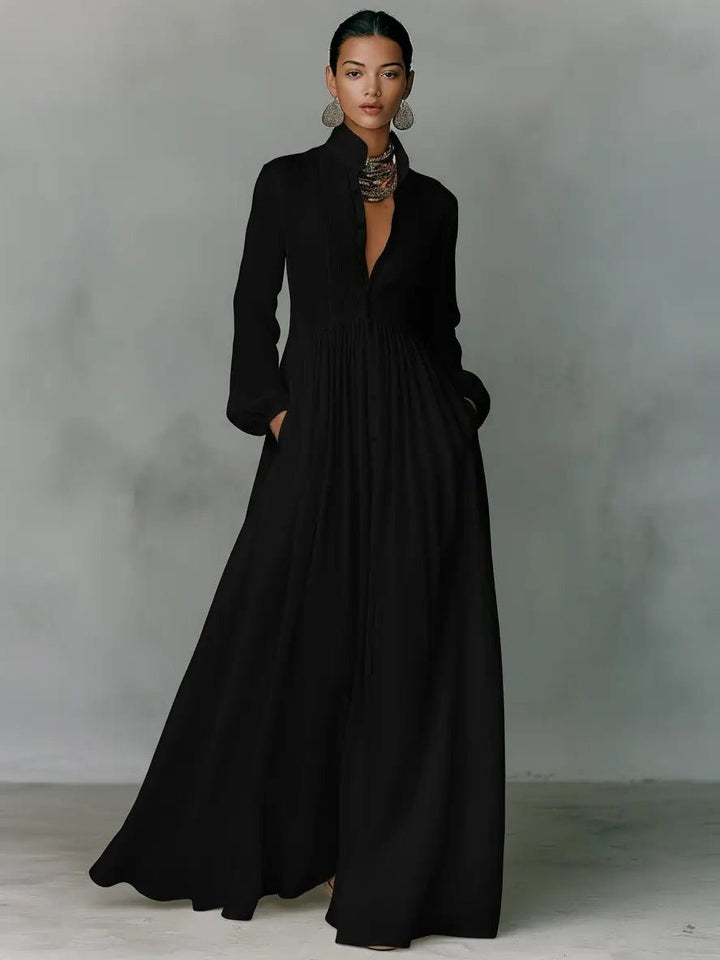 Robe maxi noire portée de face, jupe ample plissée et mains dans les poches 4