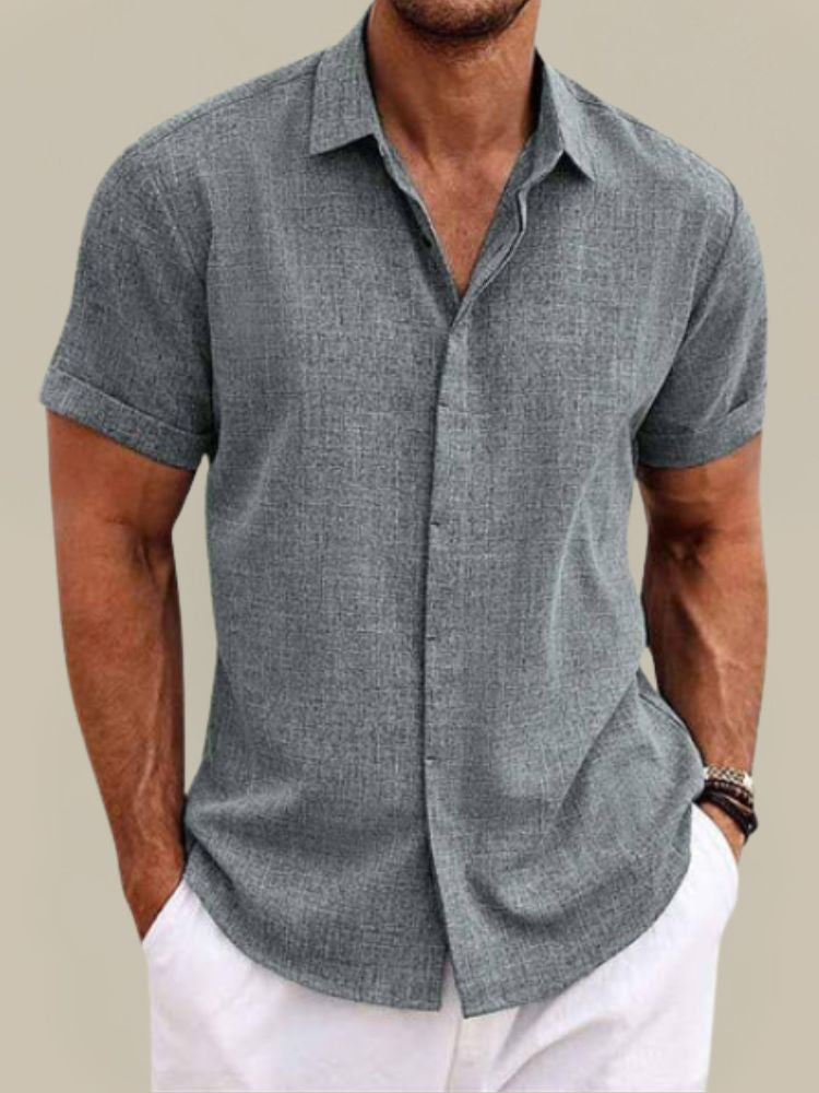 Chemise grise à manches courtes portée par un homme, tissu texturé et col chemise, avec un pantalon blanc, vue de face. 3