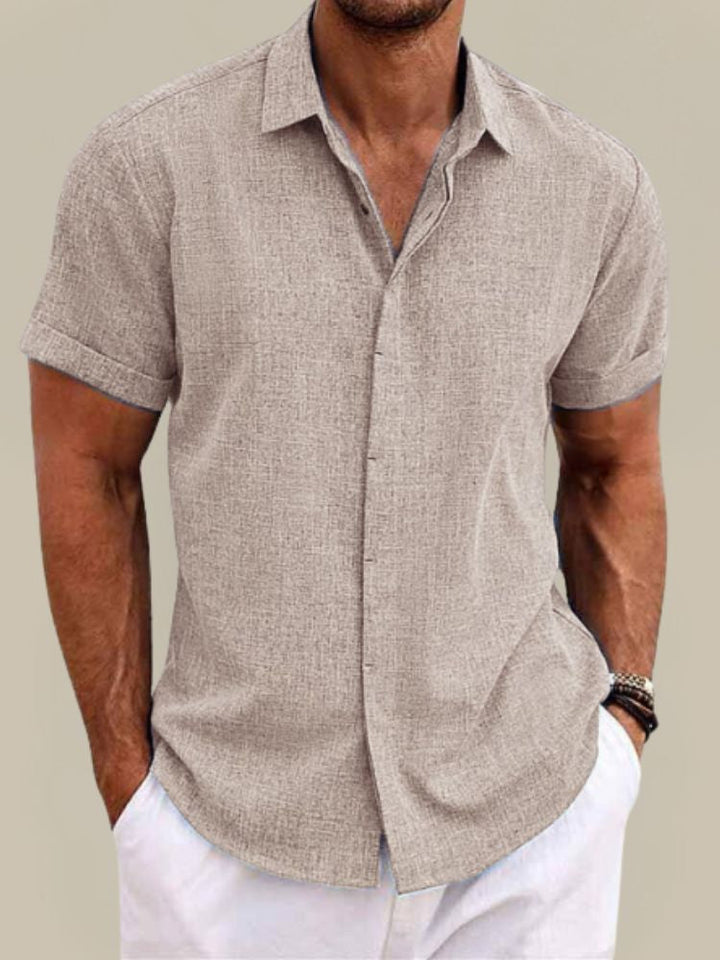 Homme en chemise beige à manches courtes retroussées, tissu texturé aspect lin, associée à un pantalon blanc, vue de face. 5