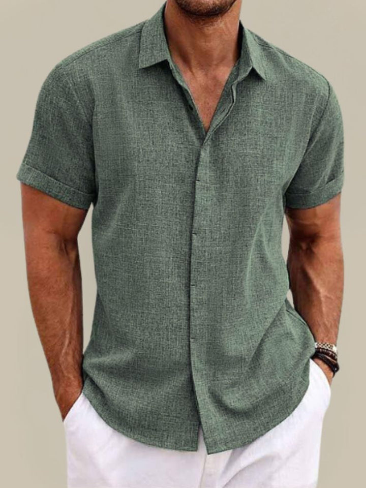 Chemise vert sauge à manches courtes portée par un homme, mains dans les poches d'un pantalon blanc, vue de face. 8