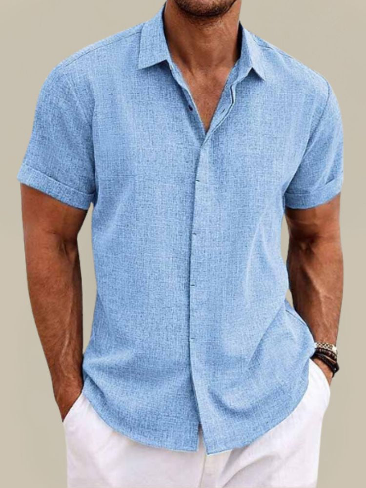Homme de face portant la chemise bleu ciel texturée, mains dans les poches d'un pantalon blanc, manches courtes retroussées. 2